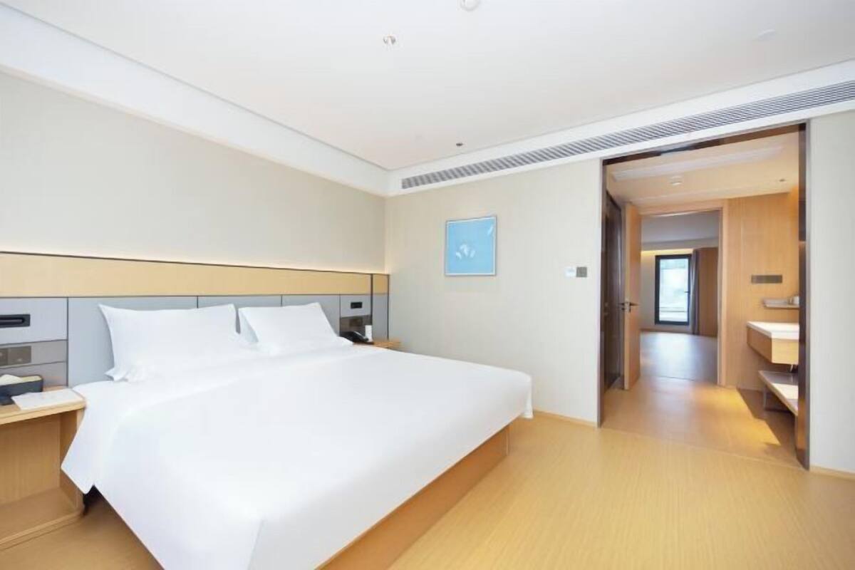 A modern hotel room with a large bed, a bedside table, and a view of the hallway.