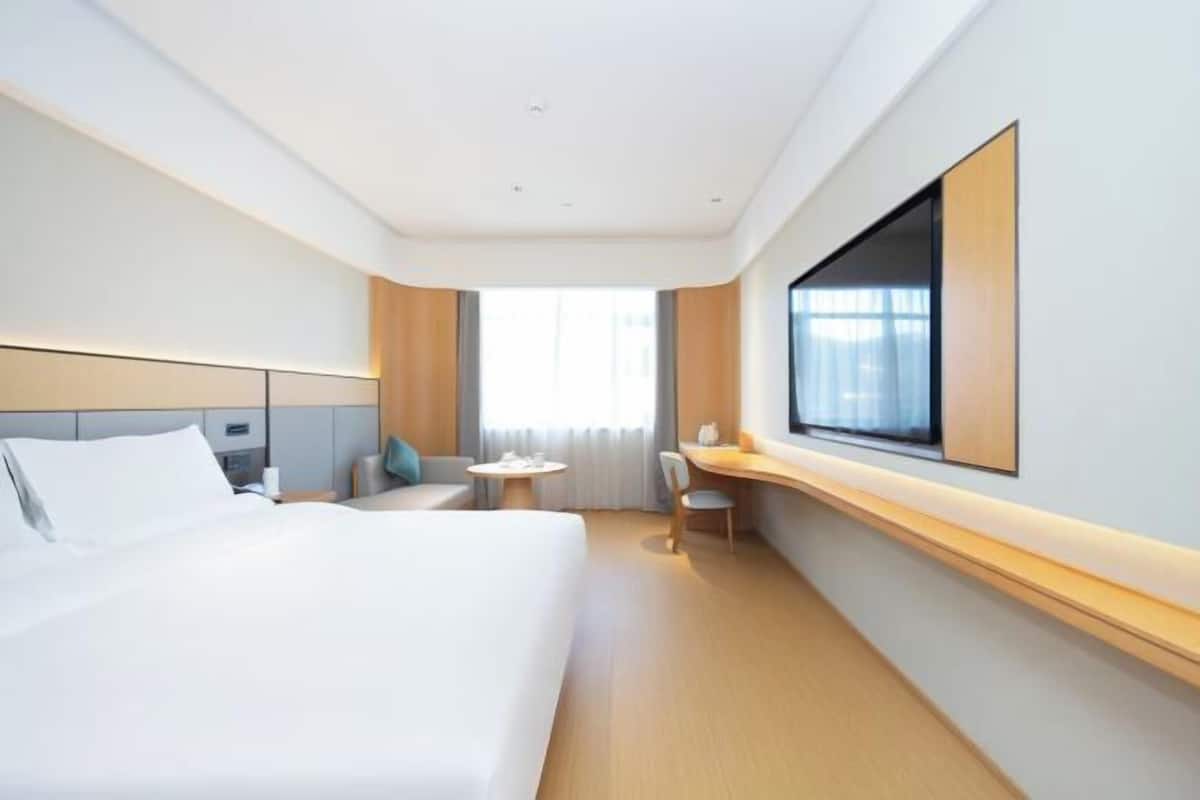 A modern hotel room with a large bed, a desk, a chair, and a TV mounted on the wall.