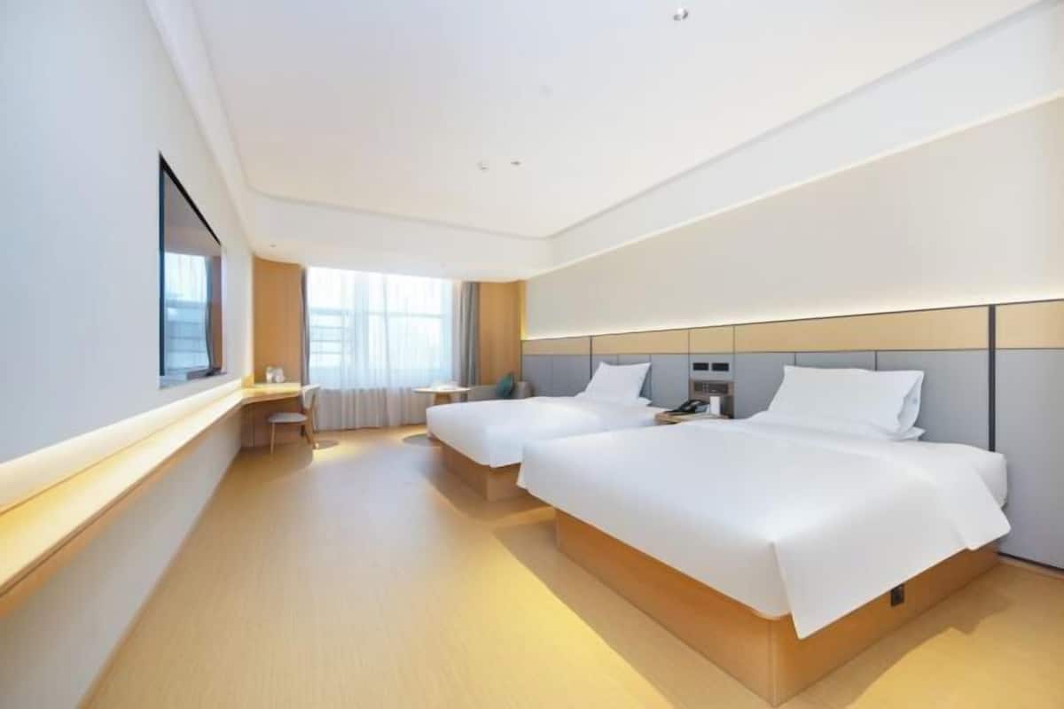 A modern hotel room with two beds, a bedside table, a chair, and a large window.