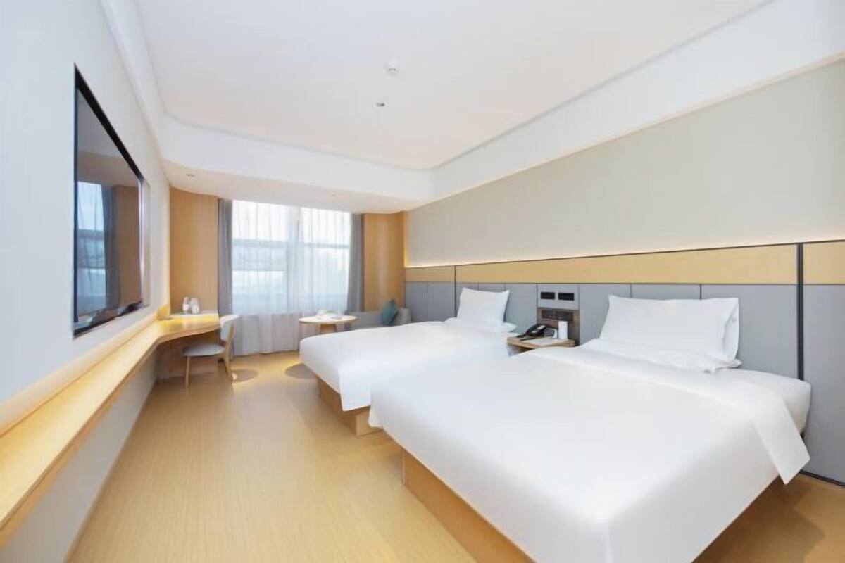 A hotel room with two beds, a desk, a chair, and a window.