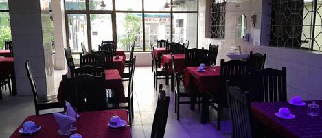 A restaurant with tables covered in red tablecloths, black chairs, and ceiling fans.