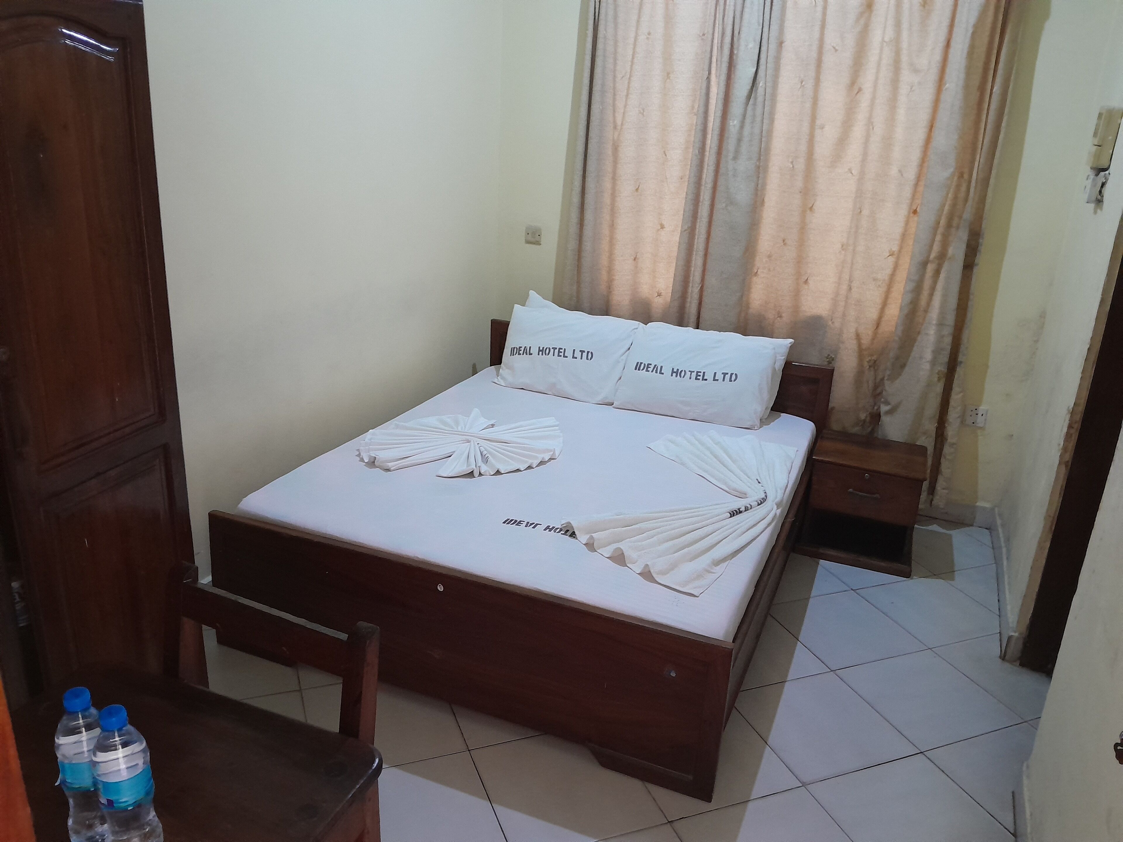 A neatly made bed with pillows labeled "Ideal Hotel Ltd." and a towel arranged on the bed.