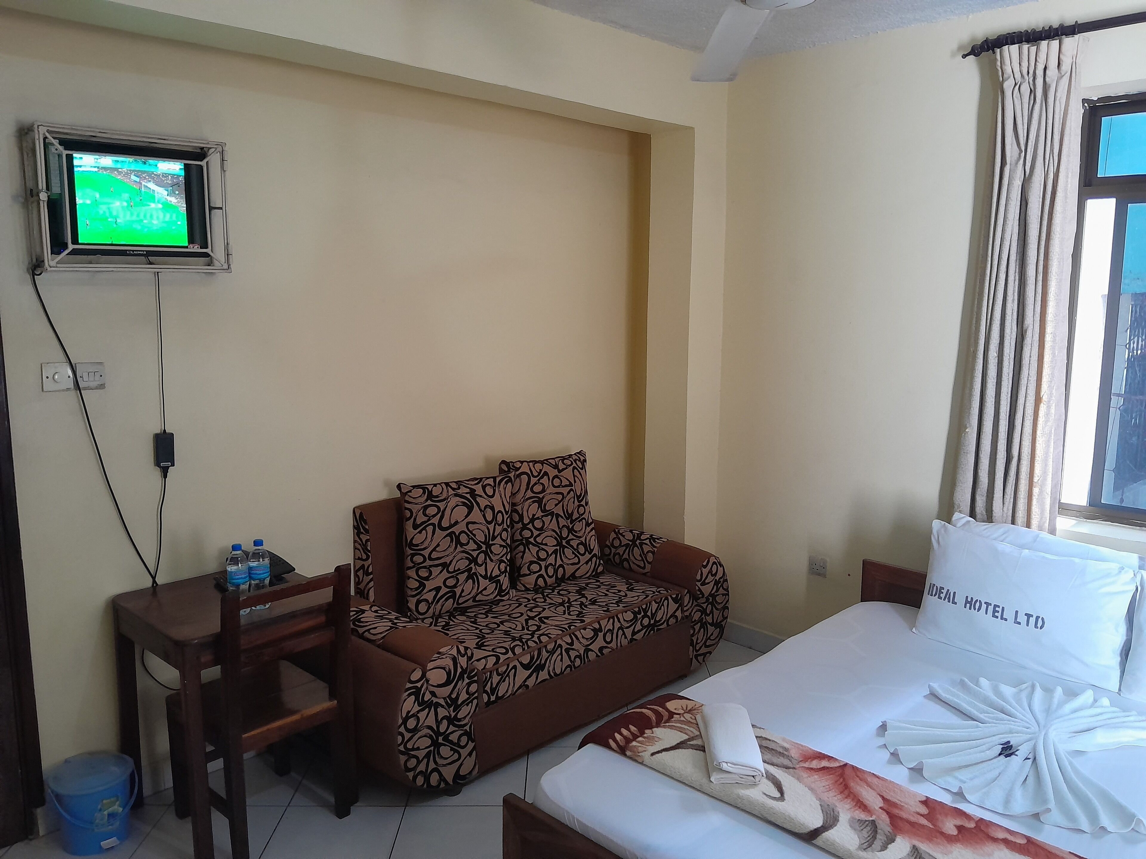 Habitación de hotel con cama, sofá, televisión en la pared y ventana con cortinas.