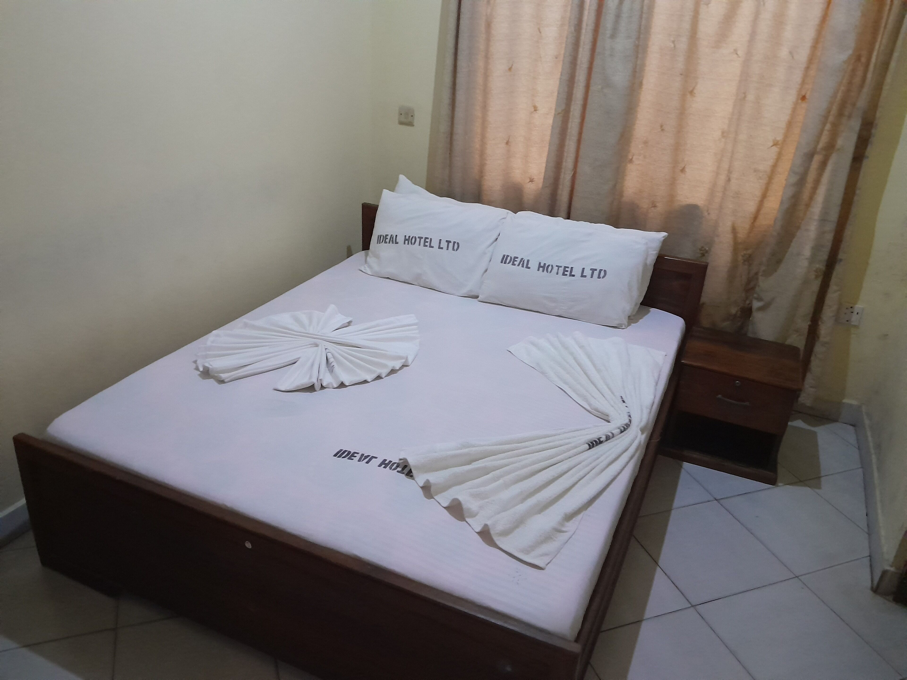 A neatly made bed with white linens and pillows labeled "IDEAL HOTEL LTD."