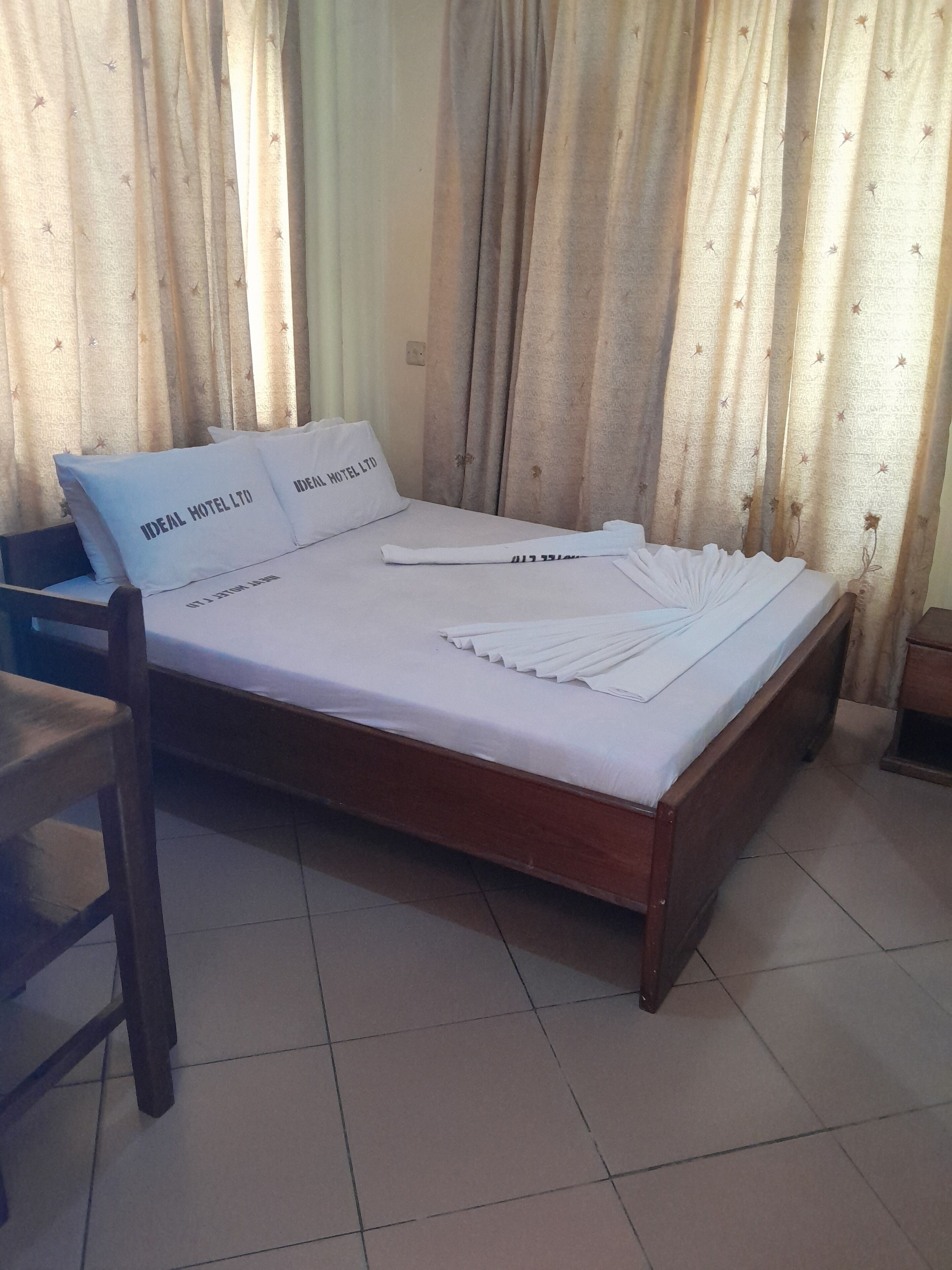 A neatly made bed with pillows labeled "IDEAL HOTEL LTD" and a folded towel.