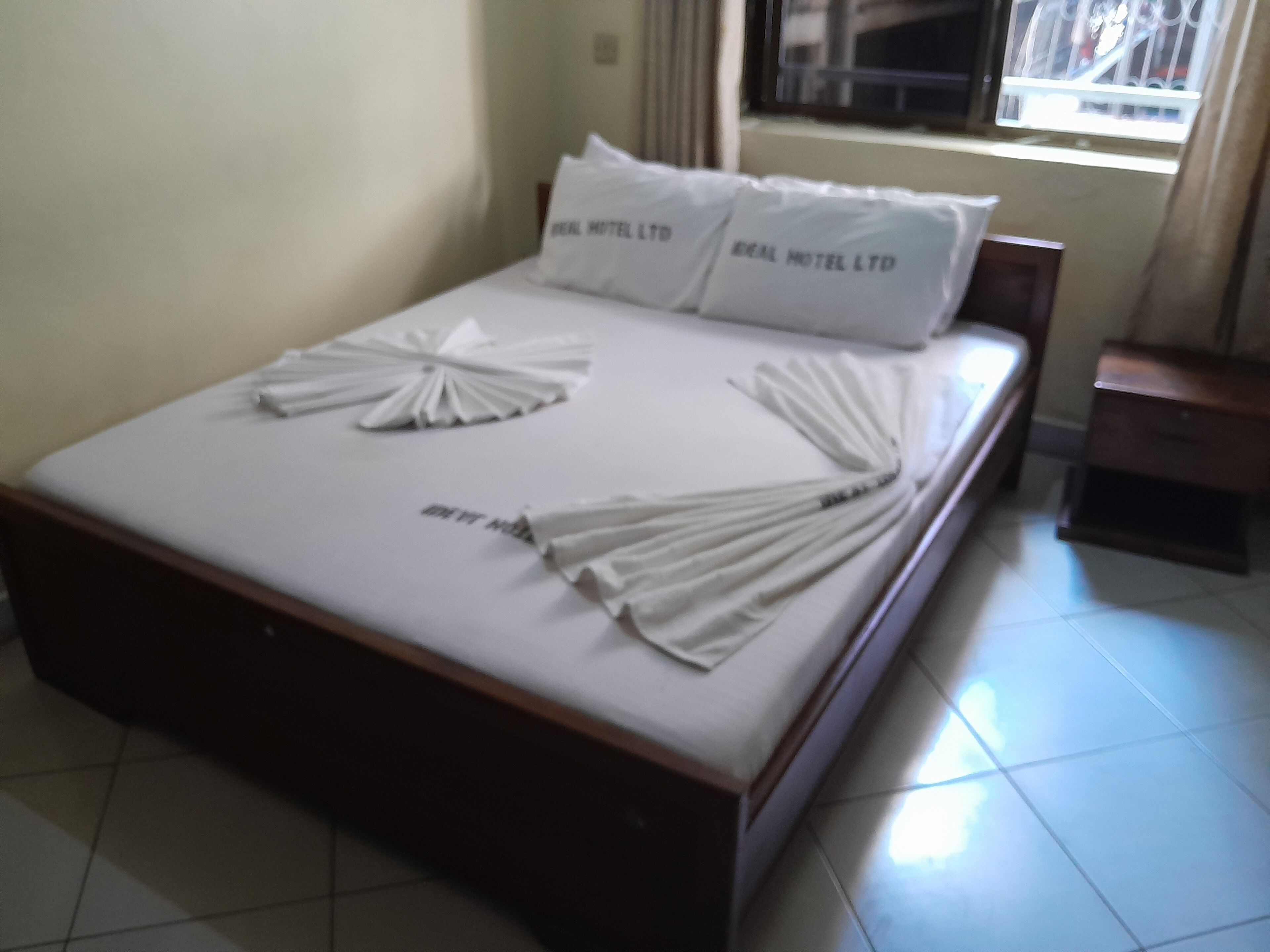 A neatly made bed with folded white towels and pillows, a wooden headboard, and a small bedside table with a lamp.