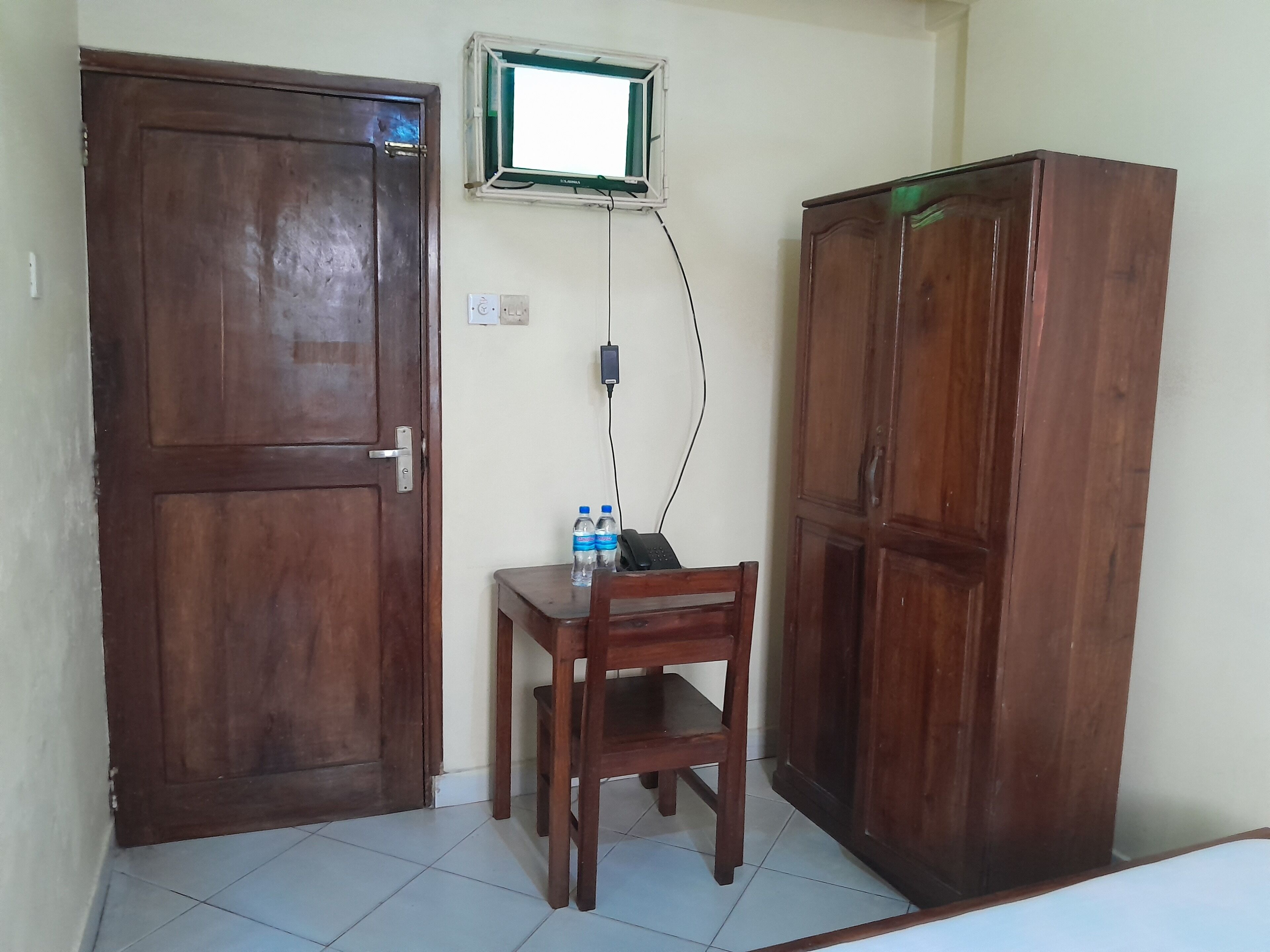 A room with a wooden door, a small table with two water bottles, a wooden cabinet, and a wall-mounted power outlet.