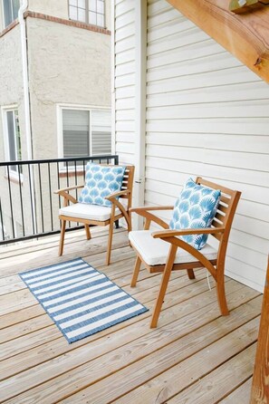 A wooden deck with two wooden chairs and a striped rug.