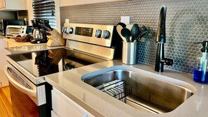 A modern kitchen with stainless steel appliances, a double sink, and a backsplash with a textured pattern. - Black Velvet King Suite in Beautiful Highland Park (Birmingham)