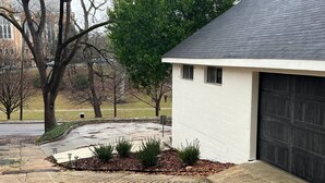 A residential driveway with a garage door, a paved area with shrubs, and a brick pathway. - Black Velvet King Suite in Beautiful Highland Park (Birmingham)