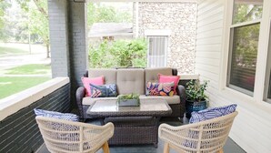 A covered porch with a sofa and two chairs, a small table, and a potted plant. - Black Velvet King Suite in Beautiful Highland Park (Birmingham)