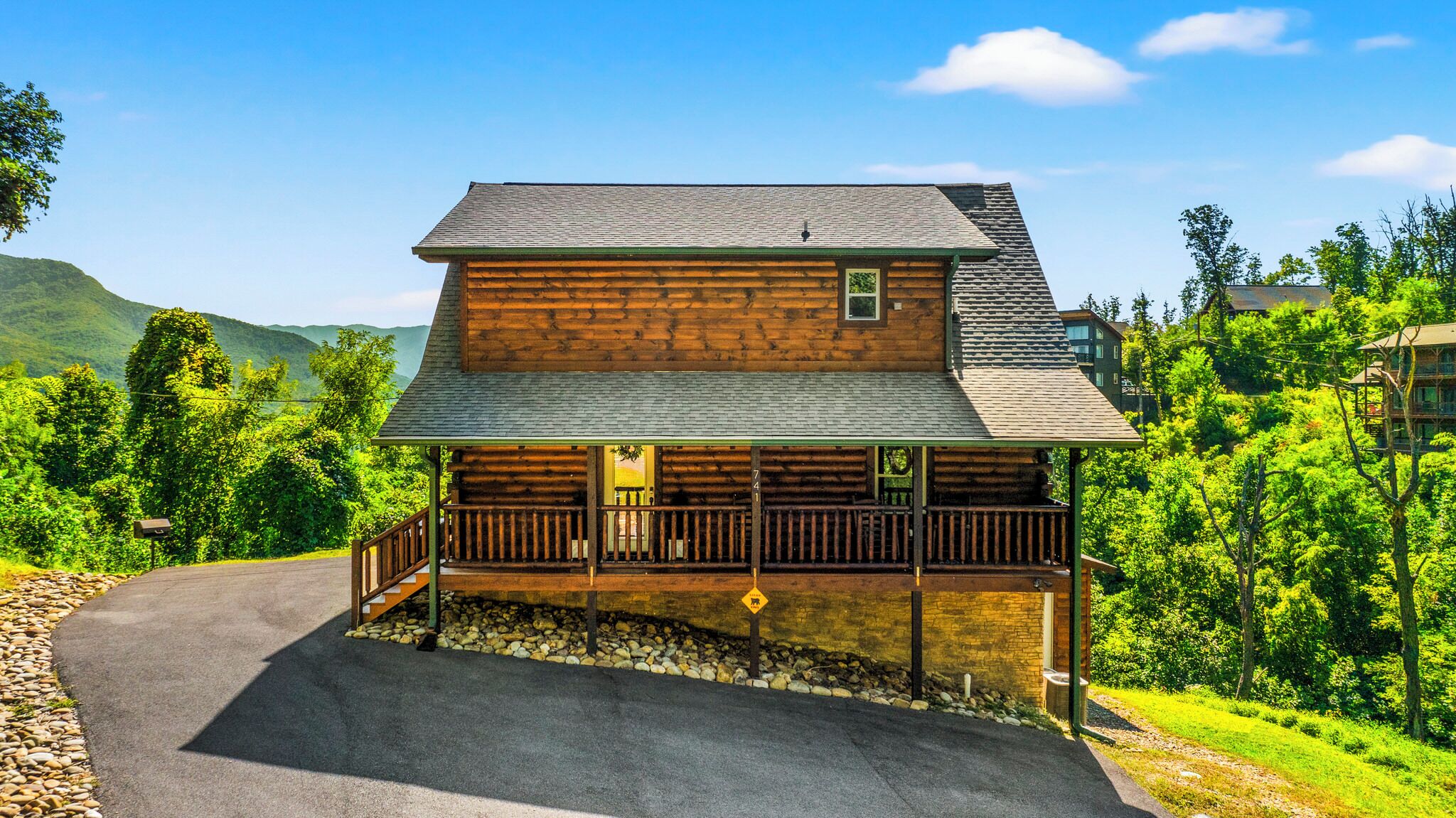 A log cabin with a porch, a stone pathway, and a mountain backdrop.