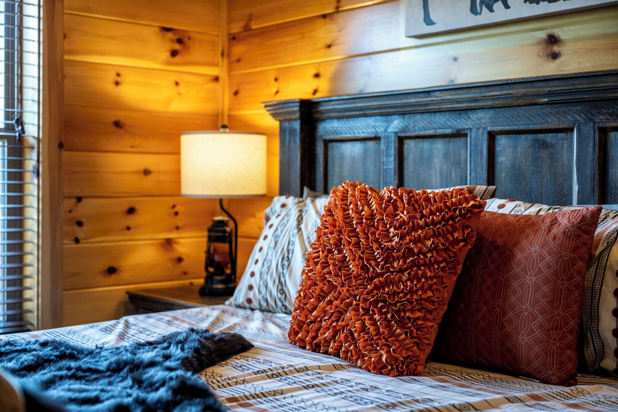 A wooden cabin-style room with a bed, a nightstand, a lamp, and a wall with a picture.