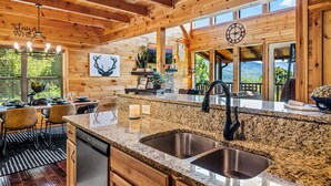 L’intérieur d’un chalet en bois comprend une cuisine dotée de plans de travail en granit, d’éviers en acier inoxydable et d’un coin repas avec une table et des chaises.