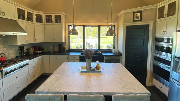 A modern kitchen with a central island, white cabinetry, stainless steel appliances, and pendant lighting.