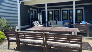 A covered patio with a table and benches, a grill, and a sofa with cushions.