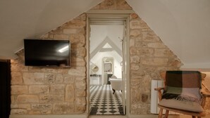 Une pièce avec un mur en pierre, un téléviseur fixé au mur, un sol à carreaux et une chaise en bois.