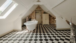 Une pièce avec un sol à carreaux noirs et blancs, une baignoire blanche et un mur en pierre.