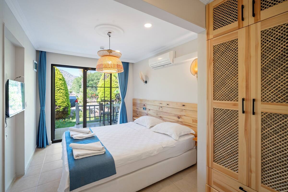 A hotel room with a bed, a balcony, a wooden wardrobe, and a ceiling light.