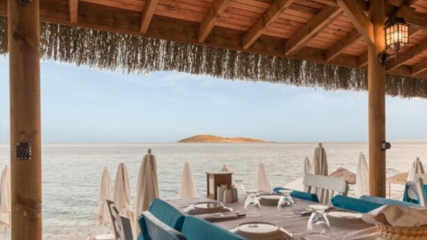 Zona pranzo sulla spiaggia con tavoli apparecchiati per due, con vista sul mare.