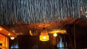 Zona pranzo all'aperto con tetti in paglia, tavoli di legno e luci appese.