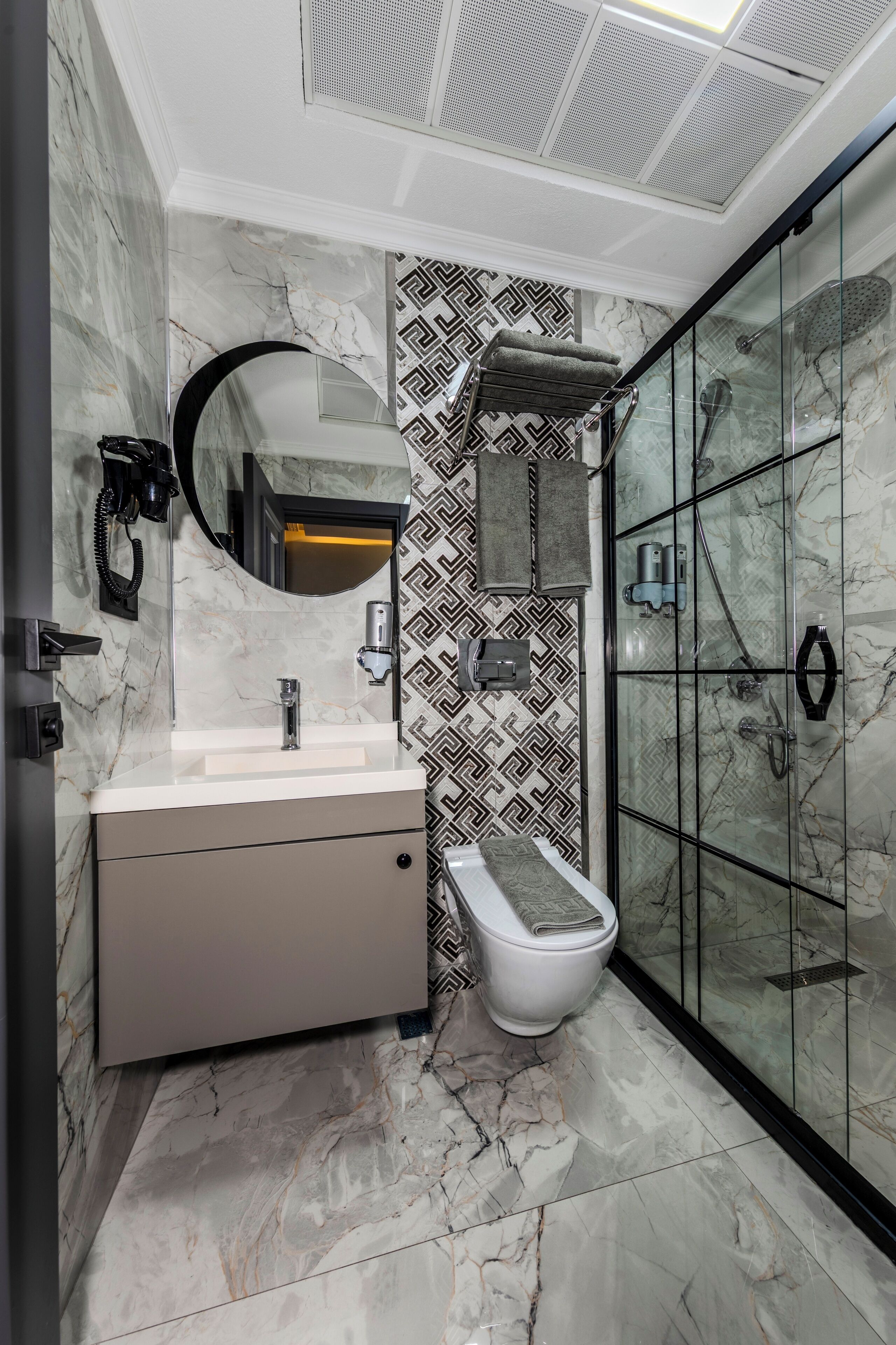 A modern bathroom with a marble floor, a glass shower enclosure, and a vanity with a mirror.