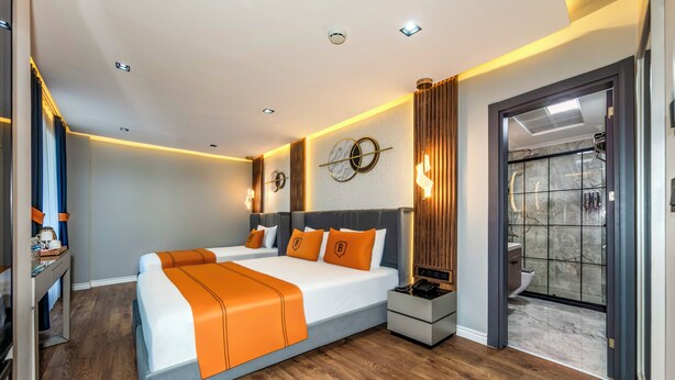 A modern hotel room with a large bed, bedside tables, a desk, and a bathroom visible through an open door. - AirGate Airport Hotel (Arnavutköy)