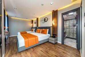 Quarto de hotel moderno com uma cama grande, mesas de cabeceira, uma escrivaninha e um banheiro visível por uma porta aberta.