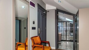 A hallway with a wooden chair, a door, and a view into a room with a tiled floor. - AirGate Airport Hotel (Arnavutköy)