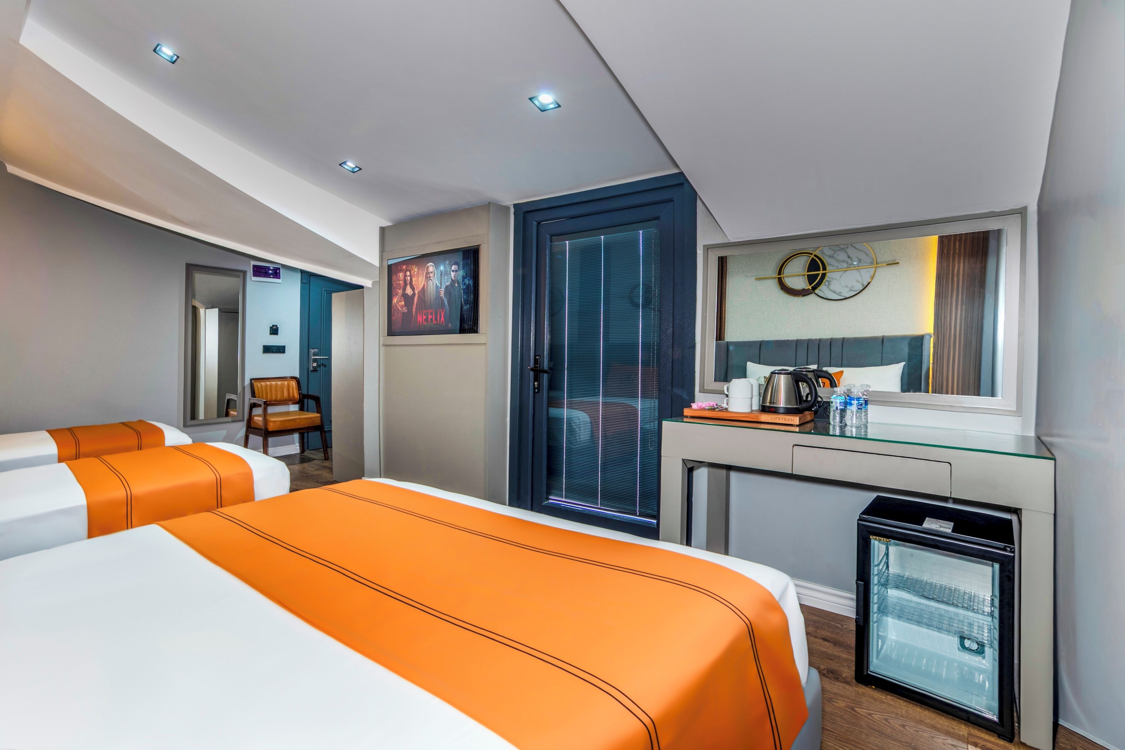 A hotel room with two beds, a desk, a minibar, and a refrigerator.