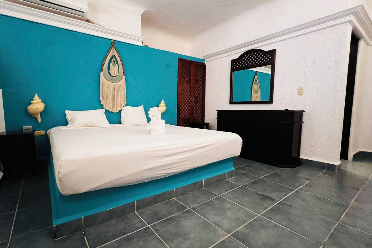 Une chambre d’hôtel avec un lit, une table de chevet, une commode, un miroir et un mur d’accent bleu.