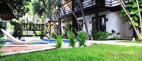 Zona de piscina con tobogán, rodeada de exuberante vegetación y un edificio blanco con balcones.