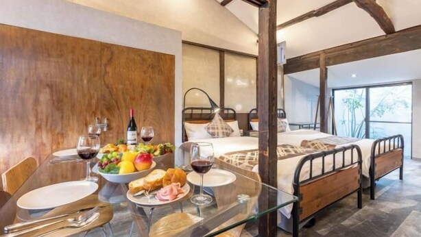 A modern room with a glass dining table set for a meal, a bed with a metal frame, and a large window offering a view. - Rent Tsuruhashi (Osaka)