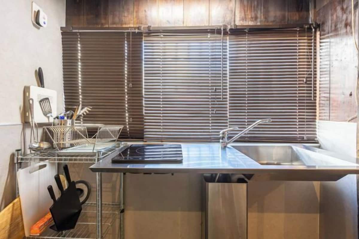 A modern kitchen with a stainless steel countertop, a built-in sink, and a window with blinds.