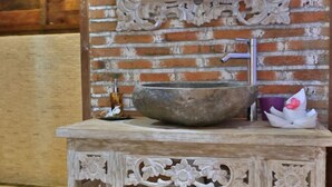 A rustic bathroom with a large stone basin, a wooden vanity, and a decorative mirror. - Villas Samalama Gili Trawangan (Gili Trawangan)