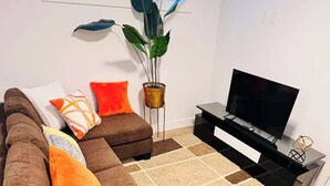 Ein modernes Wohnzimmer mit einem Ecksofa, einem Couchtisch, einem Fernsehschrank und einer großen Pflanze.