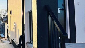 Ein Gebäude mit schwarz-weißer Fassade, einem sichtbaren Adressschild und einer Betontreppe mit schwarzer Geländer zum Eingang.