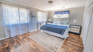 A bedroom with a bed, a nightstand, a dresser, and a window with curtains. - Beach Daze Duplex! Natural Light! Fenced Yard! Dogs Welcome! 5 blocks to beach!  (Carolina Beach)