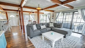 A spacious living area with a large gray sectional sofa, a white coffee table, and a patterned rug. There is a kitchen area with a blue refrigerator and wooden flooring. - Beach Daze Duplex! Natural Light! Fenced Yard! Dogs Welcome! 5 blocks to beach!  (Carolina Beach)