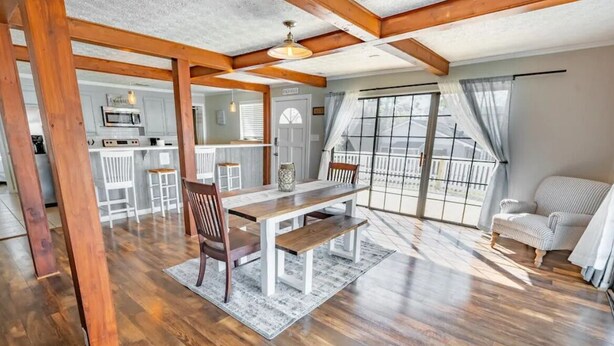 A spacious living area with a wooden dining table, a sofa, and a view of the outdoors through large windows. - Beach Daze Duplex! Natural Light! Fenced Yard! Dogs Welcome! 5 blocks to beach!  (Carolina Beach)