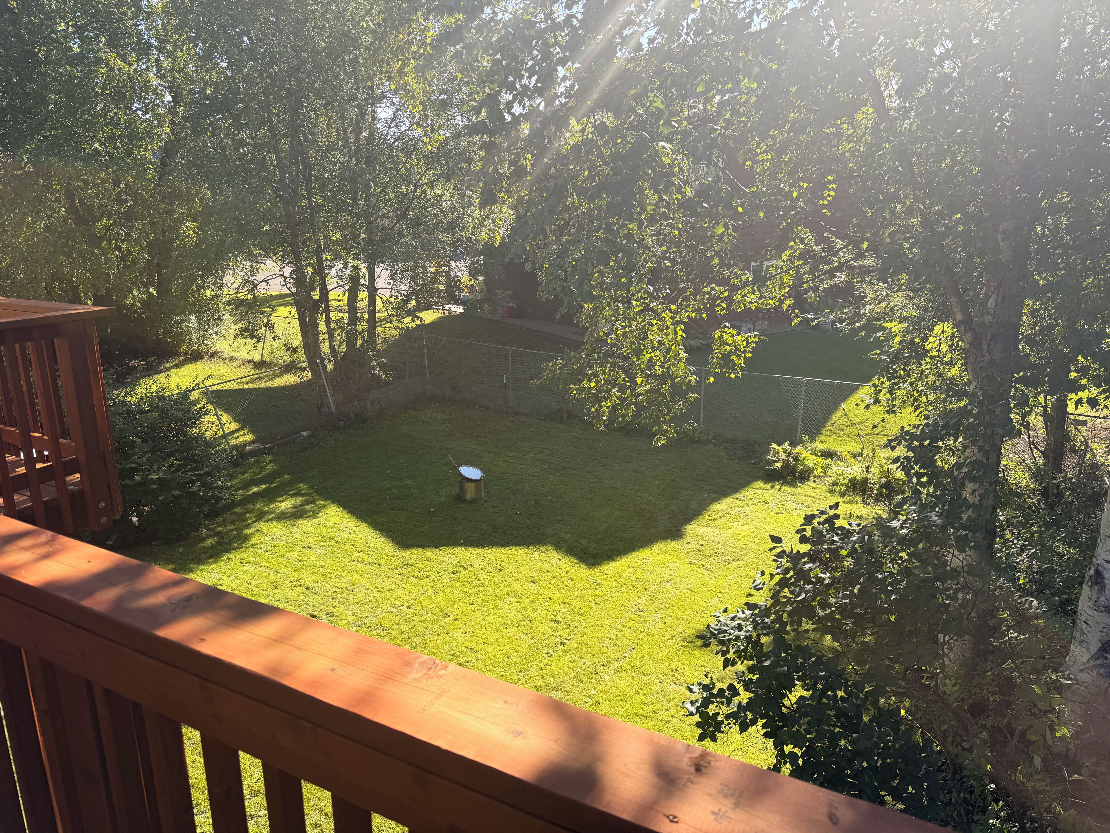Un jardin avec une pelouse, un objet en métal et une terrasse en bois.