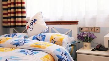 A neatly made bed with patterned bedding, a bedside table with a phone and a potted plant, and a striped curtain.