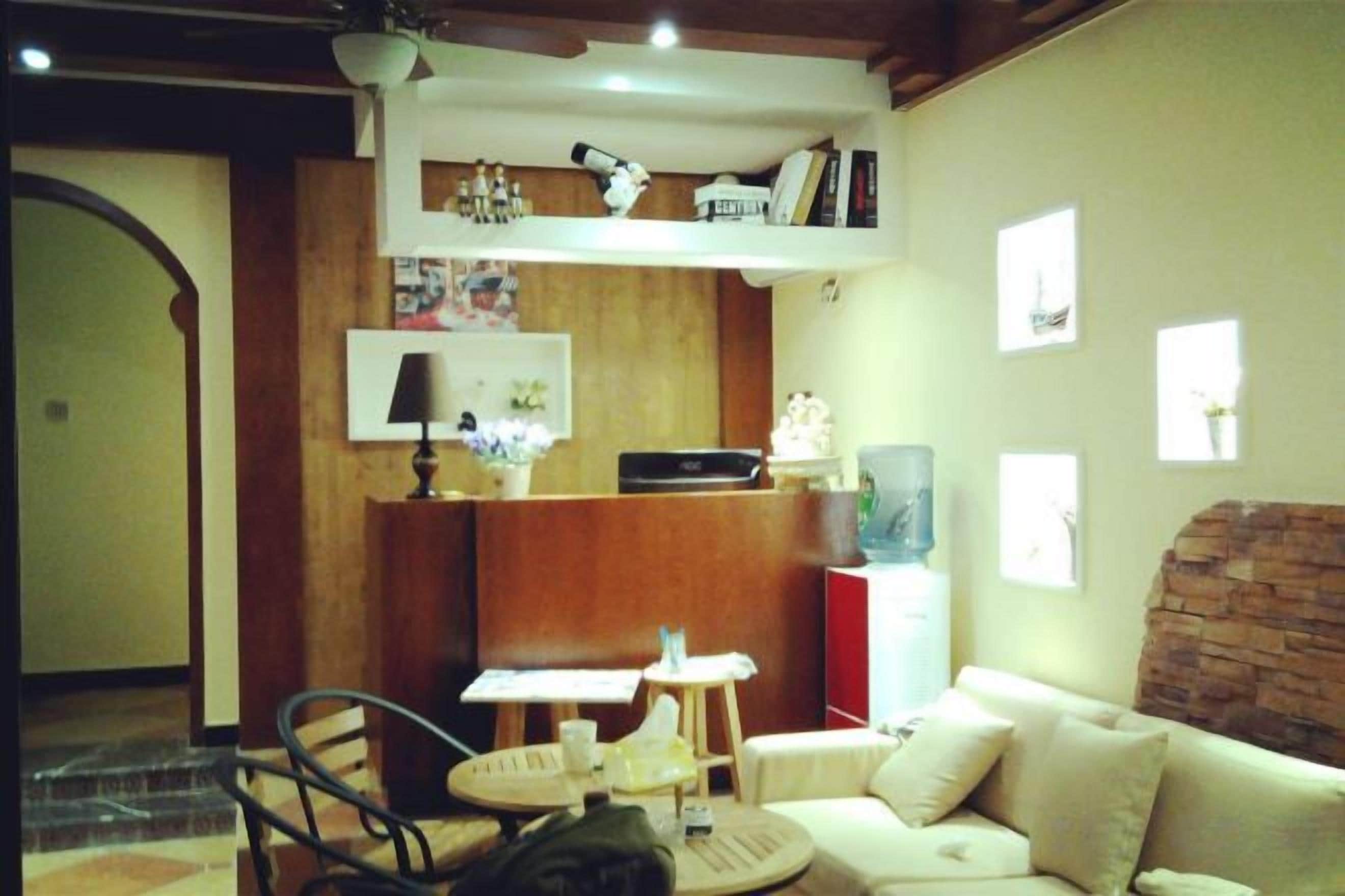 Zona d'estar acollidora amb un sofà, una taula de cafè i una taula petita amb una làmpada. Hi ha una fusta receptora amb una làmpada i una prestatgeria amb llibres i objectes decoratius.
