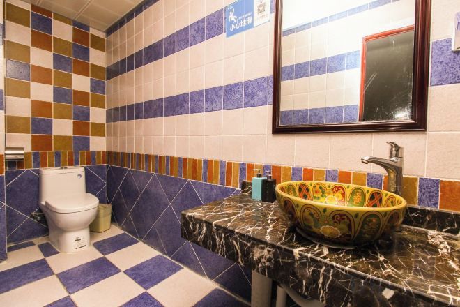 A bathroom with a checkered floor, a toilet, a sink with a decorative basin, and a mirror with a red frame.