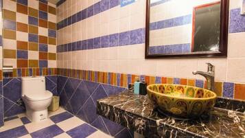 A bathroom with a checkered floor, a toilet, a sink with a decorative basin, and a mirror with a red frame.