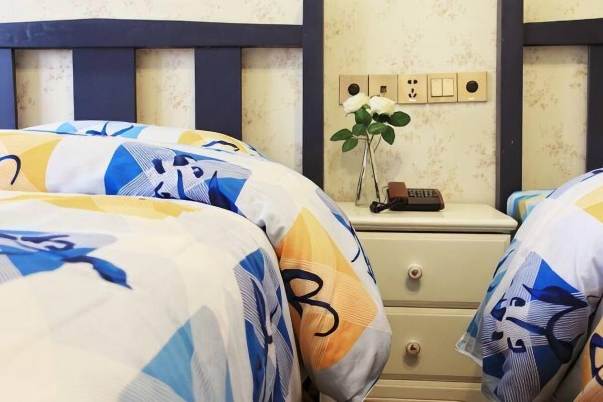 Une chambre avec deux lits, une table de chevet avec une horloge et un interrupteur fixé au mur.