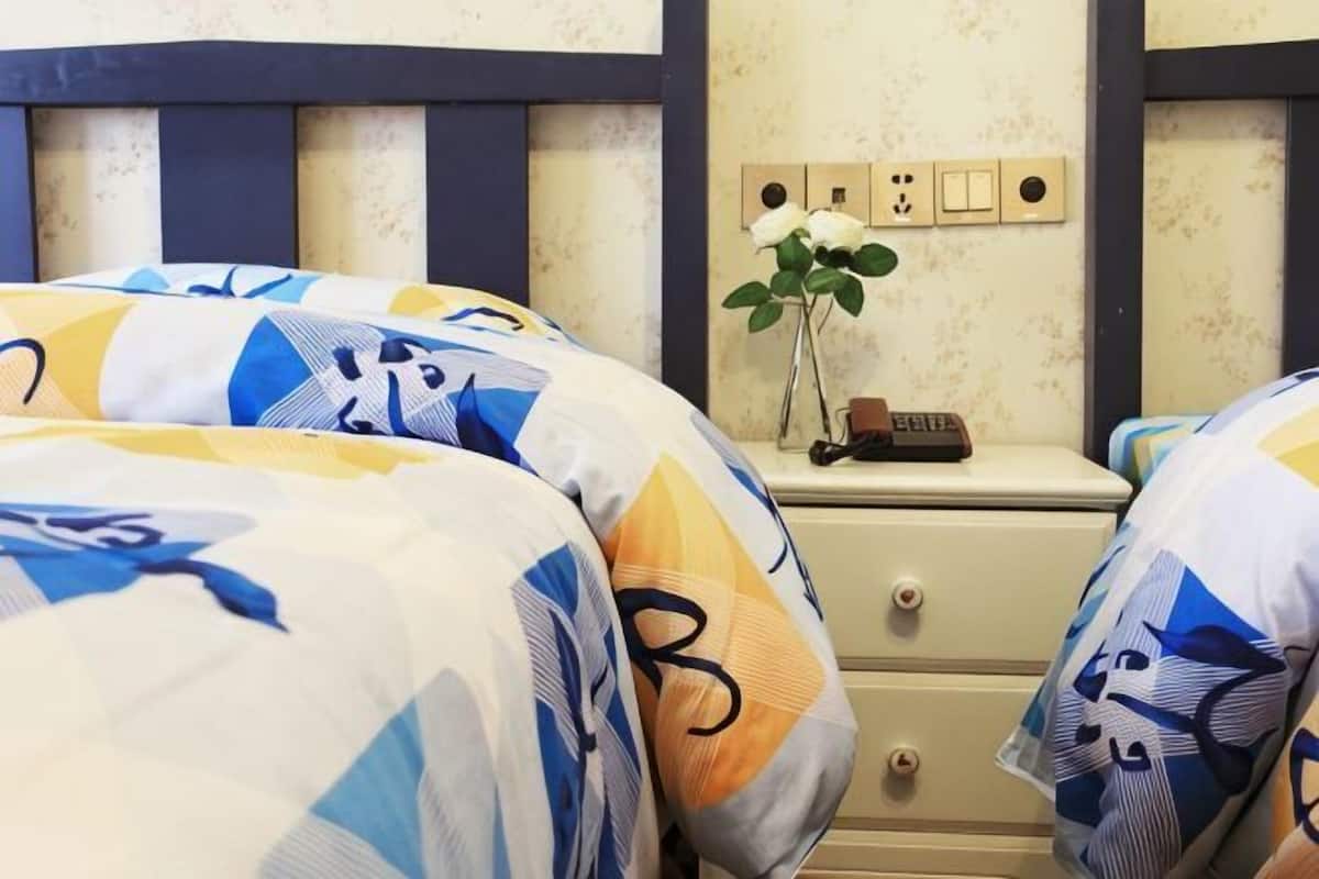 A bedroom with two beds, a nightstand with a clock, and a wall-mounted light switch.