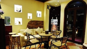 A cozy lounge area with a sofa, two round tables, and bar stools. There are framed pictures on the wall and a clock. - Laimi Theme Inn (Zhangjiajie)