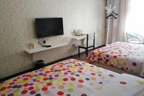 Une chambre d’hôtel avec deux lits, un téléviseur fixé au mur, une petite table avec une tasse et une soucoupe, et un porte-manteau.