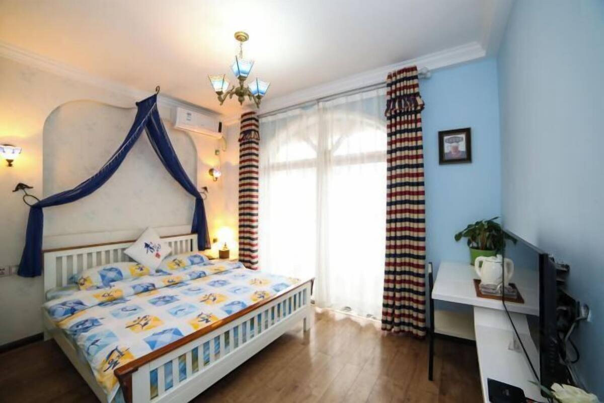 Une chambre à coucher comprenant un lit, un bureau, une chaise, une fenêtre avec des rideaux et un lustre.